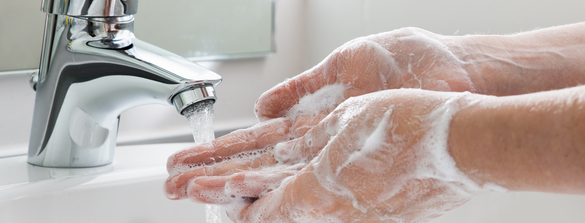 person washing their hands with foaming soap over a sink with water running