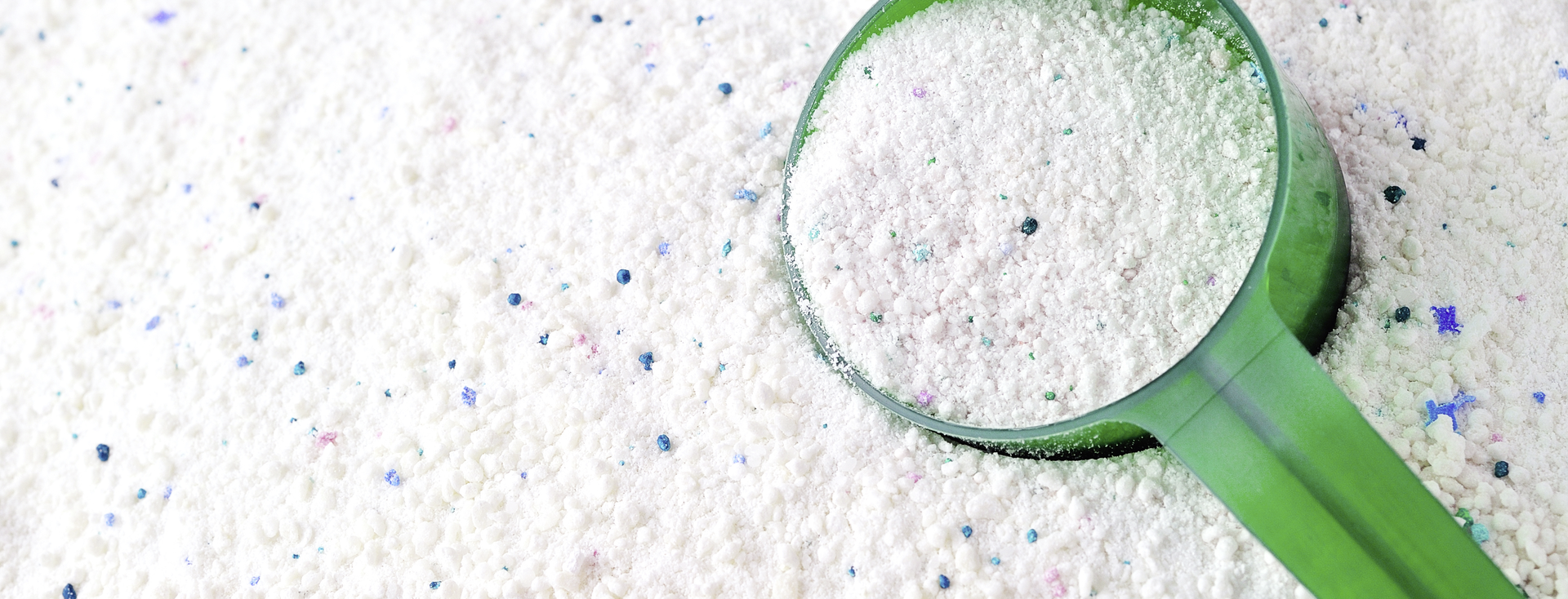Grüne Schaufel mit weißem Waschpulver, das bunte Pellets enthält Grüne Schaufel mit weißem Waschpulver, das bunte Pellets enthält