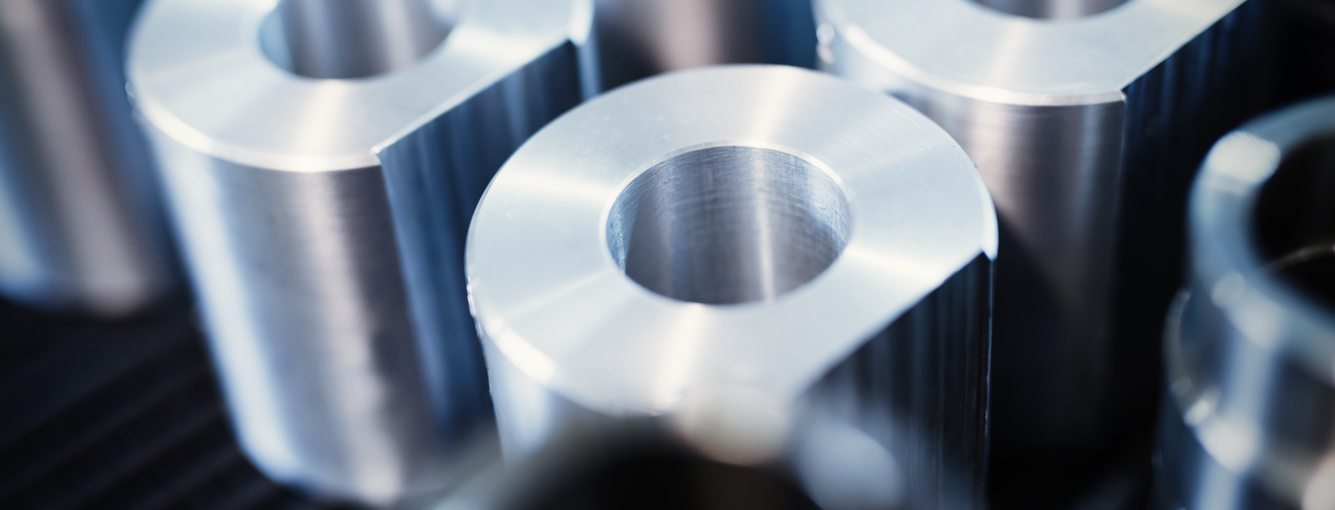 Nahaufnahme von metallisch glänzenden, zylindrischen Präzisionsteilen mit Bohrungen Nahaufnahme von metallisch glänzenden, zylindrischen Präzisionsteilen mit Bohrungen