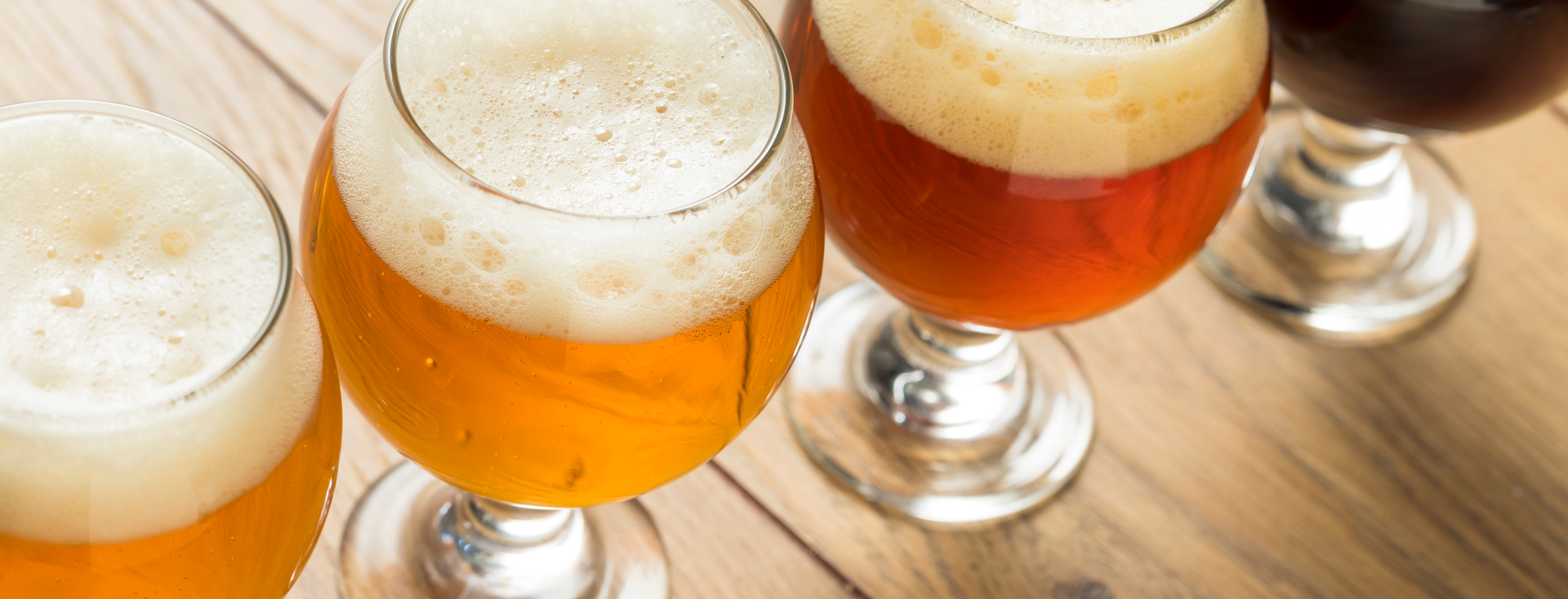 4 glasses of foamy beer in varying shades of color