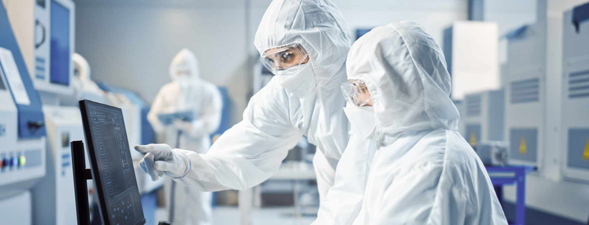 two engineers in cleanroom suits are working on a computer to control a machine