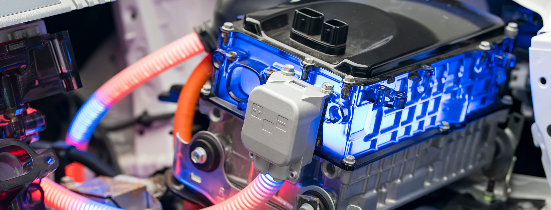 Nahaufnahme eines elektrischen Antriebsstrangs mit blau leuchtenden Komponenten und orangefarbenen Kabeln Nahaufnahme eines elektrischen Antriebsstrangs mit blau leuchtenden Komponenten und orangefarbenen Kabeln